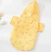 Small dog wearing a bright yellow short-sleeve summer raincoat outdoors.

