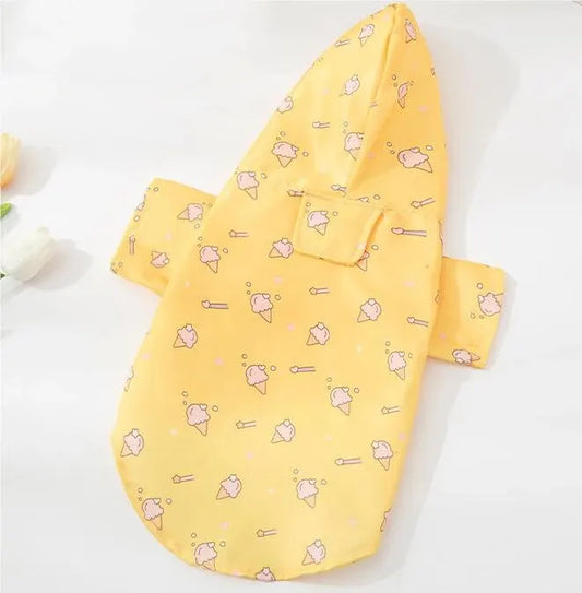 Small dog wearing a bright yellow short-sleeve summer raincoat outdoors.

